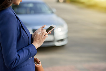Close-up shot of unrecognizable businesswoman wearing classical jacket using smartphone while standing at roadside