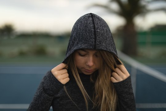 Woman standing in hoodie at tennis court