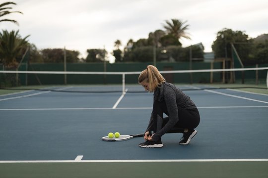Young woman tying her shoelaces in tennis court
