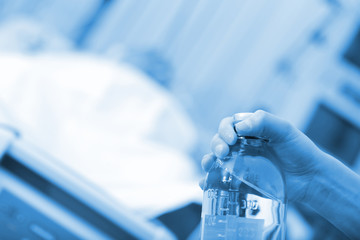 Female nurse hands with saline bottle on the background of sleeping patient in the emergency room