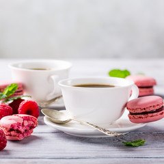 Cup of coffee with french raspberry macaroons cookies on vintage white background. Holidays food concept. Copy space.