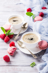 Cup of coffee with french raspberry macarons cookies on old white background. Holidays food concept.
