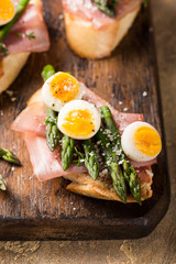 Easter breakfast or lunch with sendwich with ham, asparagus and quail eggs on old wooden chopping board. Spring food concept.