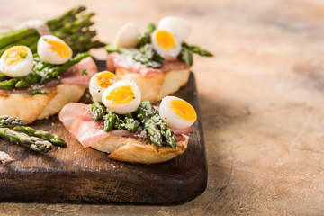 Easter breakfast or lunch with sendwich with ham, asparagus and quail eggs on old wooden chopping board. Spring food concept with copy space.