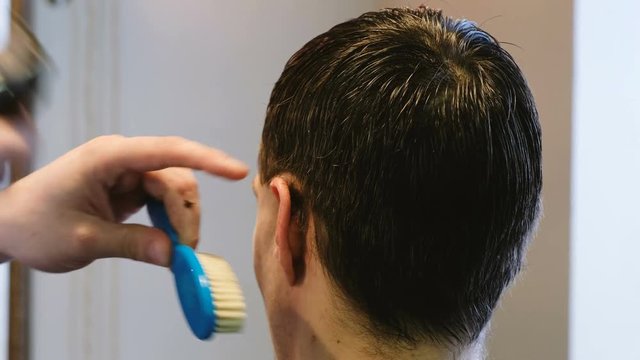 Hairdresser equates hair with an electric razor behind the ear of a man in barbershop