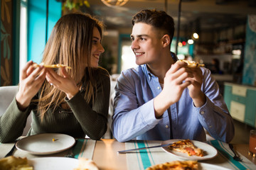 Portrait of an happy couple.They are laughing and eating pizza and having a great time in cafe.