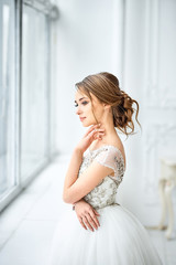 Wedding. Bride in a beautiful dress indoors in a white studio, like at home.  the bride looks out the window.