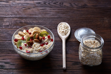 Composition with bowl of oatmeal porrige and dry oatmeal in glassware on vintage wooden table, selective focus