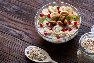 Composition with bowl of oatmeal porrige and dry oatmeal in glassware on vintage wooden table, selective focus