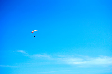 Paragliding over the ocean on the island of Bali. The blue sky shimmers with the blue ocean. The parasutists fly high above the precipice like birds. Aerial view with copy space