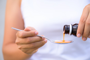 Woman pouring medication or antipyretic syrup from bottle to spoon. healthcare, people and medicine concept.