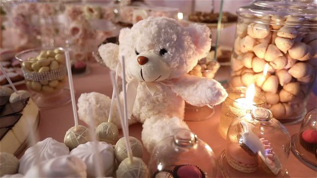  Children's party. Candy bar in the restaurant, children's party, birthday, a white teddy bear with a butterfly on her neck, lit candle, teddy bear on a table Candy bar, close-up