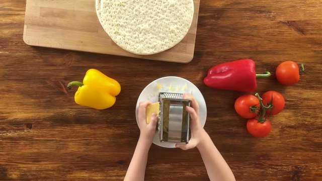 Little boy is making pizza, scrape cheese with grater, top view video