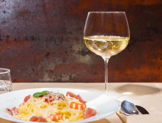 Close up of glass with wine near tasty spaghetti pasta in white plate on decorated table with light tablecloth