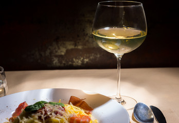 Close up of glass with wine near spaghetti pasta in white plate on decorated table with light tablecloth