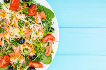 Close up of appetizing salad with shrimps, grated cheese, mix of lettuce leaves, olives in white plate