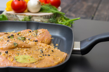 Close up of marinated chicken meat on a grill pan near pepper, onions, tomatoes, dill and parsley on a wooden board