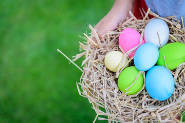 A kid holding Colorful of Easter eggs in nest on grass green background.