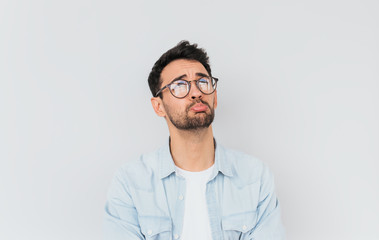 Horizontal portrait of stressed frustrated man curves lower lips isolated over white studio background. Bearded male having sad expression wearing blue shirt on white T-shirt. People, emotions concept