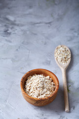 Oat flakes in bowl and wooden spoon isolated on white background, close-up, top view, selective focus.