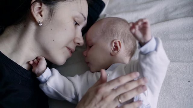 Mother with baby in bed is pressed. Mother and newborn baby. Happy mother and child kissing and hugging. Motherhood is a beautiful, happy family shots.