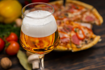 Glass of beer and appetizing pizza with salami on background
