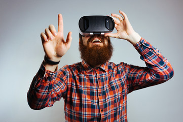 Amazed bearded man wearing virtual reality goggles and touching air.  Smartphone using with VR headset. Studio horizontal shot.