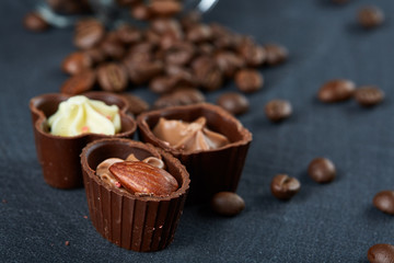 Side view of overturned glass jar with coffee beans and chocolate candies on wooden background, selective focus