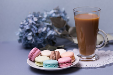 Close-up morning glass cup of coffee with milk, cake macaron and flower on blue table. Beautiful dessert.