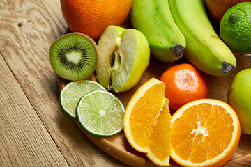 Ripe fresh fruits in a wooden plate on a light wooden background, selective focus, close-up, top view