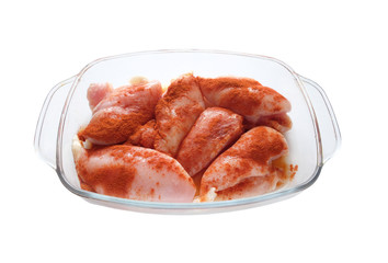 Many raw juicy cutted chicken fillets pink pieces well sprinkled with red pepper inside square transparent bowl isolated on white are ready for baking front view closeup
