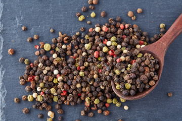 Top view on composition of peppercorns in wooden spoon on dark background, close-up.
