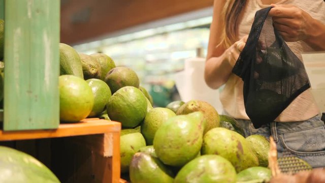 Vegan Zero Waste Girl Choosing Fresh Avocados in Supermarket. Young Mixed Race Woman Shopping without Plastic Bags in Grocery Store. 4K.