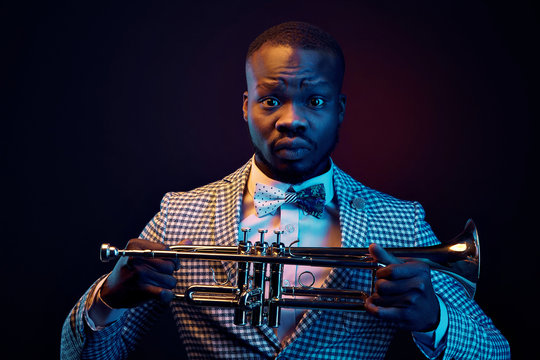 Neon portrait of handsome black jazzman in plaid jacket with floral bow tie with trumpet in his hands. Orange and blue studio light