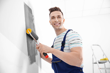 Young male decorator painting wall in room