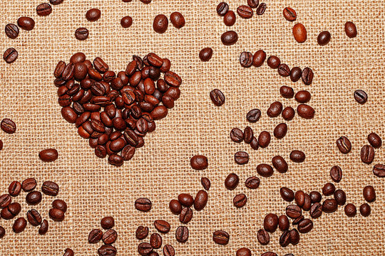 Grains of tasty roasted coffee collected in the form of a heart on a background of cloth burlap