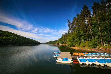 Mountain landscape with docks and pedal cycle boats on lake Gozna surrounded by forest at Valiug, Caras-Severin County, Romania