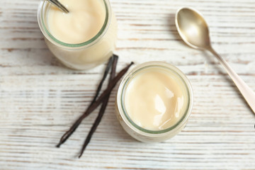 Fototapeta na wymiar Jars with vanilla pudding and sticks on wooden background