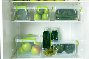 Different green vegetables and fruits in containers on shelves of refrigerator