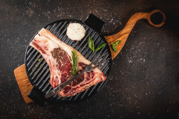 Raw beef marbled meat striplon rib eye steak with spices, grill pan, and herbs, dark background top view, copy space