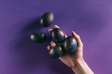 cropped image of woman holding painted easter eggs above violet surface