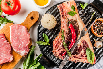 Raw beef marbled meat striplon rib eye steak with pork steaks spices, grill pan, and herbs, white marble background top view, copy space