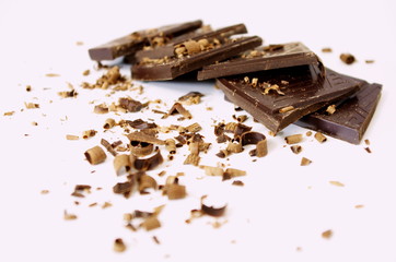 Pieces of dark chocolate bar, cubes, sprinkled with grated chocolate, on white background.
