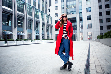 young stylish girl, passing by the Windows.Wearing fashionable glasses and a red coat. Abstract looking to the side. concept of street fashion