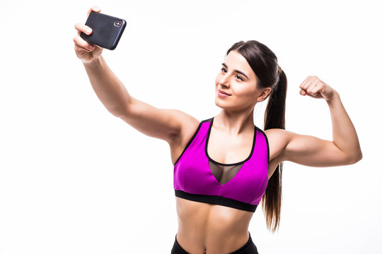 Happy sporty woman making selfie photo on smartphone and showing biceps on a white background