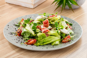 Fresh mix salad with ham and dried tomatoes on gray plate