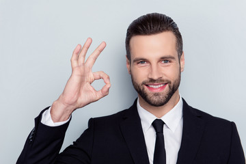 Close up portrait of cheerful excited handsome attractive friendly kind delightful with modern stylish fashionable hairstyle demonstrating ok symbol isolated on gray background
