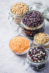 Vegan protein source, dry legumes in glass jars on stone background. Selective focus, space for text. 