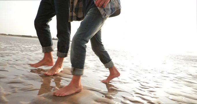 Low angle, tracking shot, of a unrecognisable child with his father walking across the beach on the wet sand.