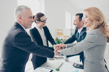 Portrait of four cheerful, stylish, successful, elegant, classic business persons in suits putting their palms on top of each other standing near desk, table in workplace, workstation